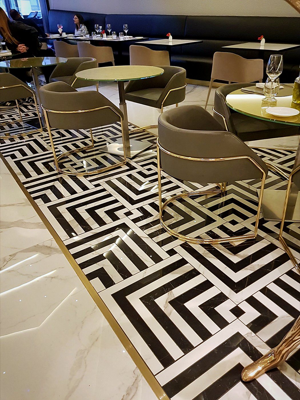 Black and white waterjet-cut marble floor in a restaurant with brass chairs